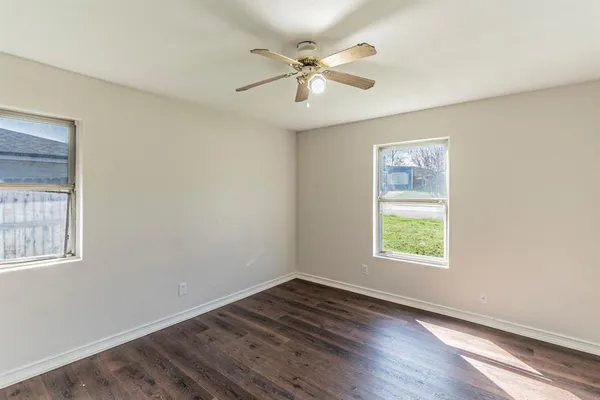 an empty room with wooden floor chandelier fan and windows