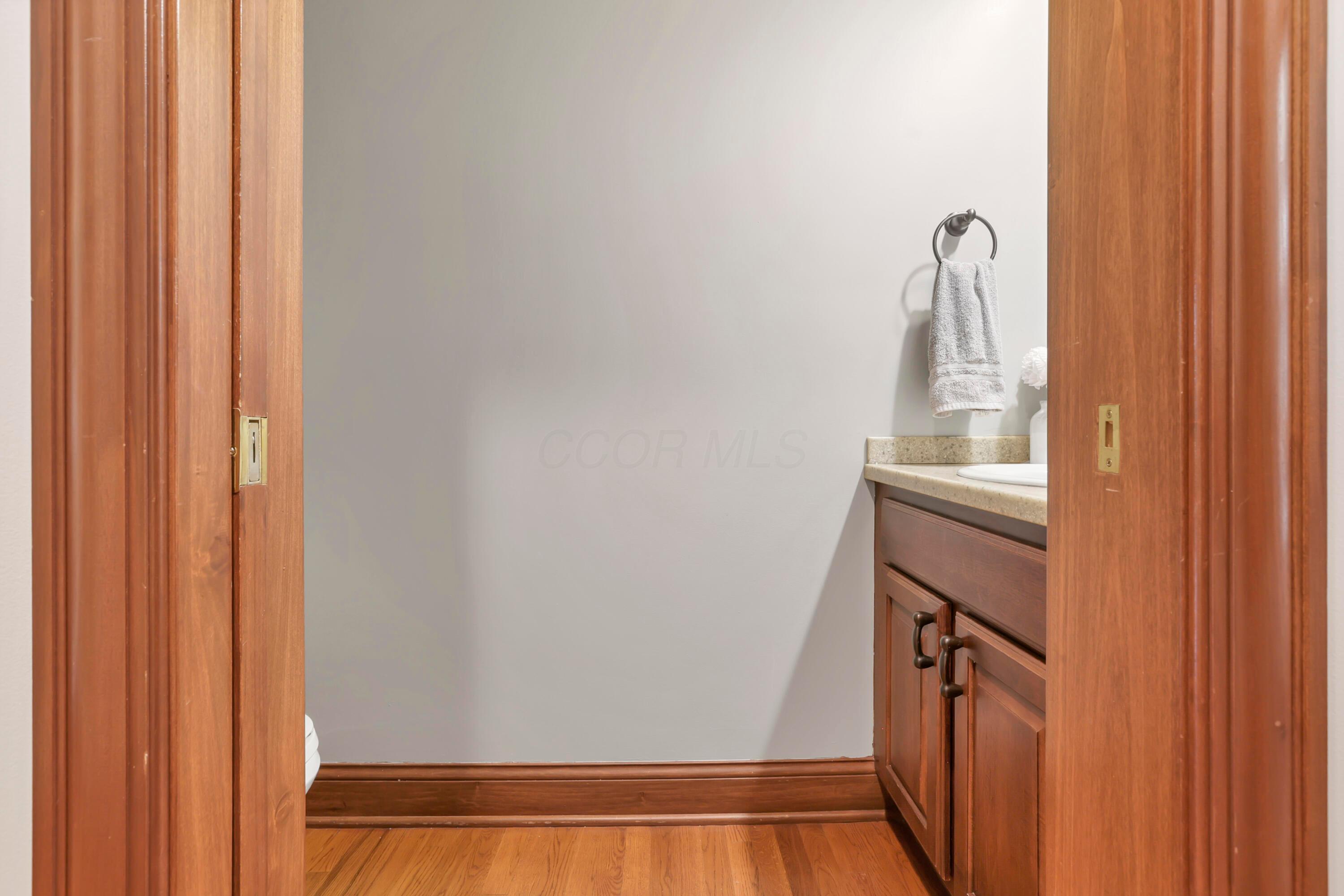 3575 State Rte 37 West Delaware, OH 43015 - Photo 73 of 106 Hardwood flooring and wood trim frame a powder room featuring a wood-finish vanity with a light-toned countertop and an integrated sink