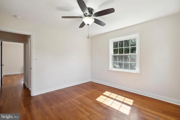 an empty room with wooden floor chandelier fan and windows