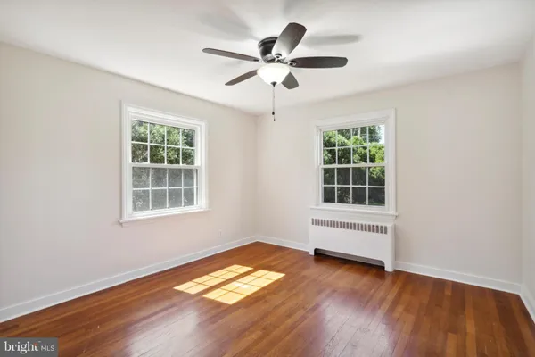 an empty room with wooden floor chandelier fan and windows