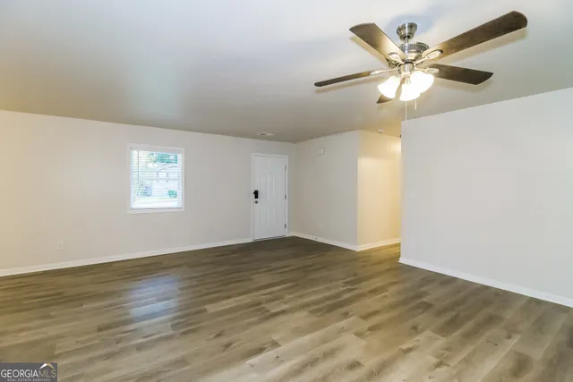 a view of an empty room with wooden floor and a ceiling fan