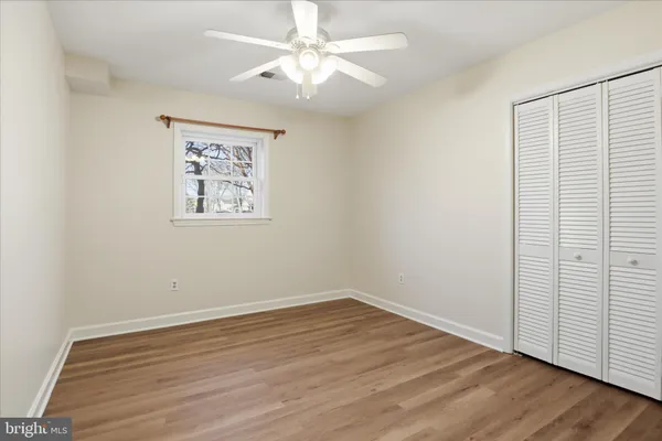 an empty room with wooden floor chandelier fan and windows