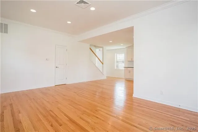 a view of an empty room with wooden floor and a kitchen