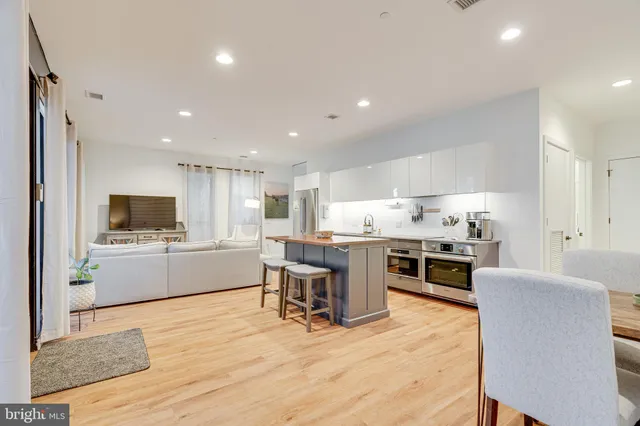 a kitchen with stainless steel appliances kitchen island granite countertop a stove top oven a sink dishwasher a dining table and chairs with wooden floor
