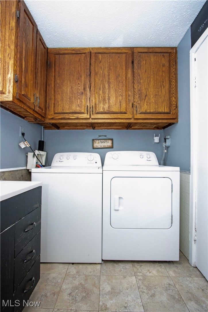 53 Grant Street Rittman, OH 44270 - Photo 23 of 34 Laundry area featuring cabinet space, a textured ceiling, washer and clothes dryer, and light tile patterned flooring