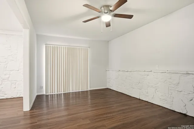 an empty room with wooden floor chandelier fan and windows