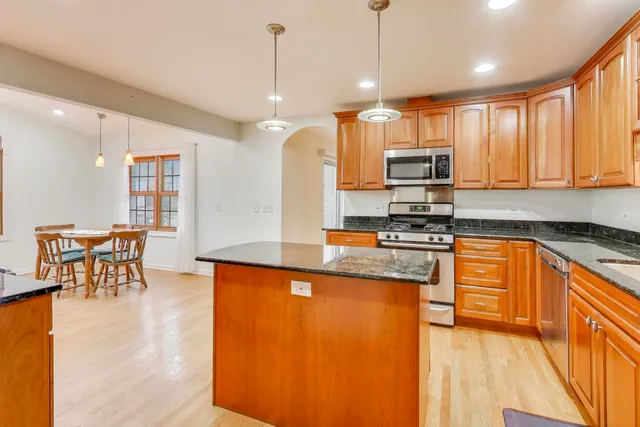 a kitchen with stainless steel appliances granite countertop a stove a sink a microwave a dining table and chairs with wooden floor