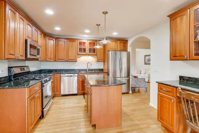 a kitchen with stainless steel appliances granite countertop a stove top oven a sink dishwasher a refrigerator and cabinets with wooden floor