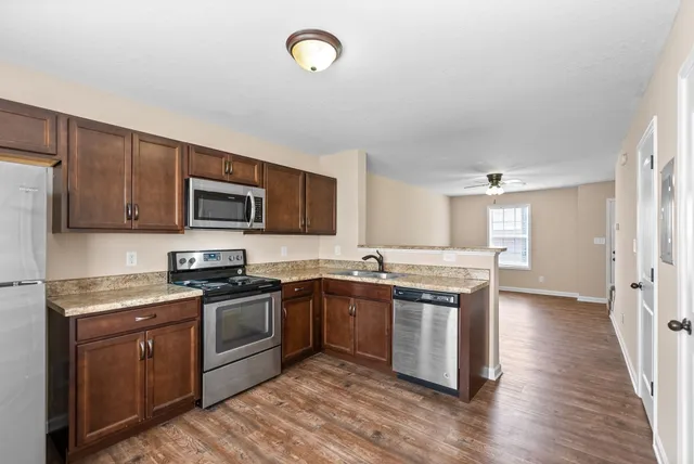 a kitchen with stainless steel appliances granite countertop a stove top oven a sink dishwasher and a refrigerator with wooden floor