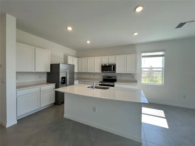 a large white kitchen with stainless steel appliances granite countertop a stove a sink a refrigerator and white cabinets with wooden floor