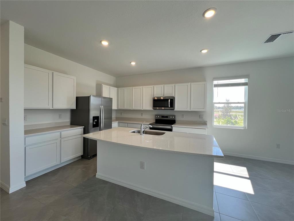 110 Mangrove Shade Circle Apollo Beach, FL 33572 - Photo 6 of 36 a large white kitchen with stainless steel appliances granite countertop a stove a sink a refrigerator and white cabinets with wooden floor