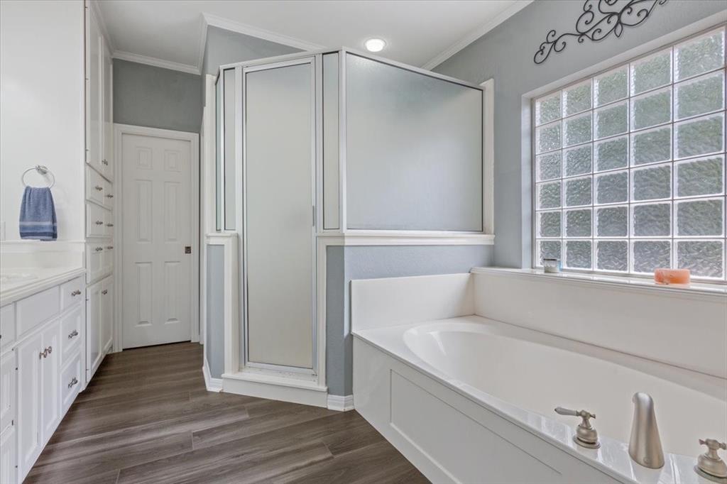 111 Spring Creek Street Waco, TX 76705 - Photo 23 of 40 Corner shower with frosted glass enclosure, soaking tub with brushed nickel fixtures, glass block window, double vanity with white cabinetry, and wood-finish flooring
