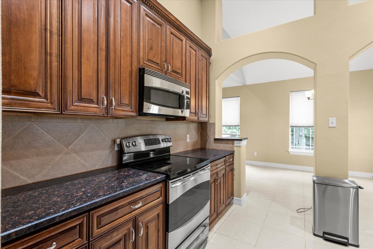 437 Balch Road Elgin, TX 78621 - Photo 10 of 37 Rich wood cabinetry and modern appliances create a practical kitchen space, opening to an airy adjacent area with high ceilings.