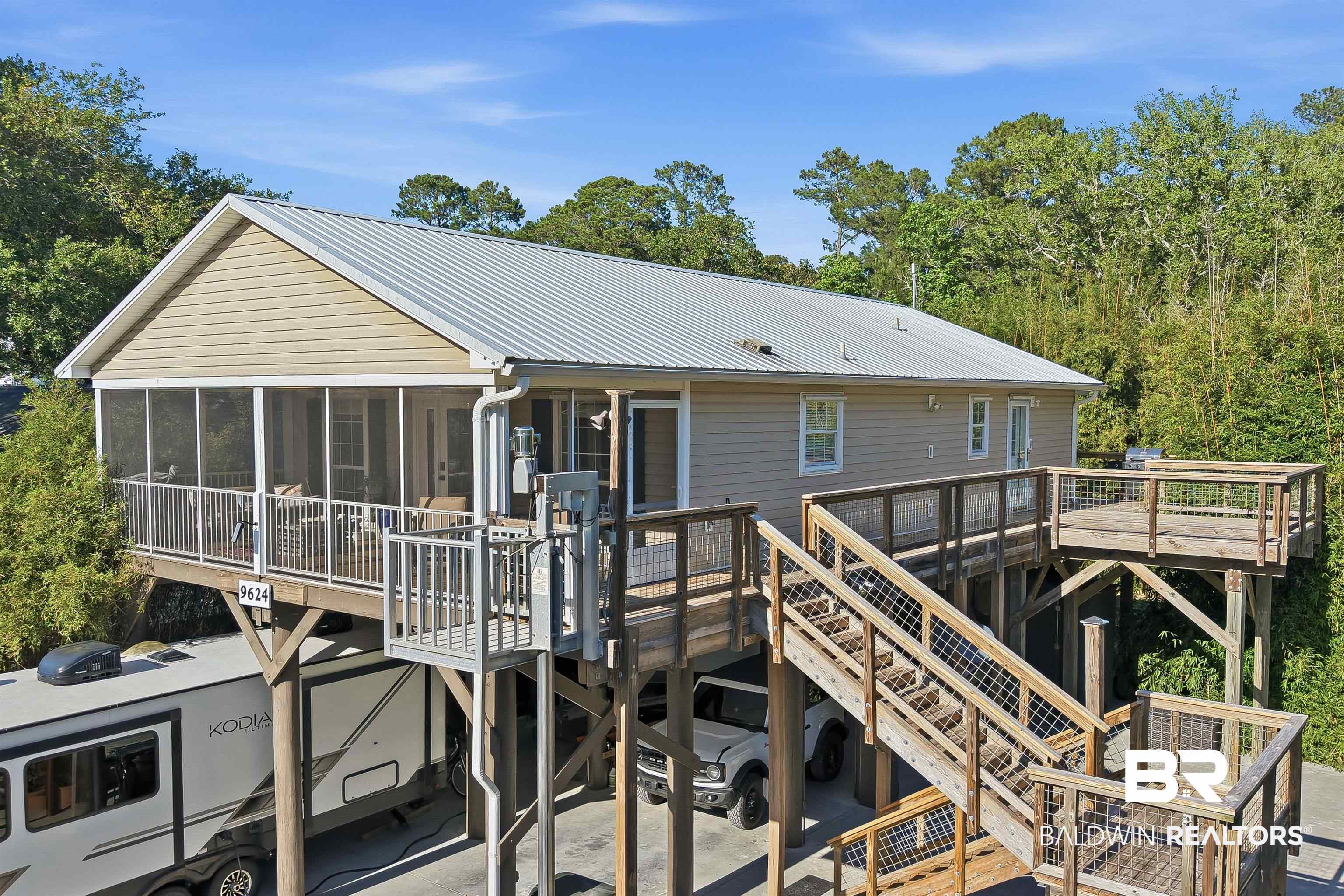 9624 North Bay Street Foley, AL 36535 - Photo 3 of 59 Elevated residence featuring a metal roof, screened porch, extensive outdoor decking, exterior lift system, and covered parking beneath