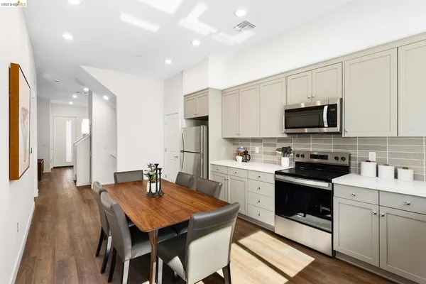 a kitchen with stainless steel appliances granite countertop a stove a sink a microwave a refrigerator and white cabinets with wooden floor