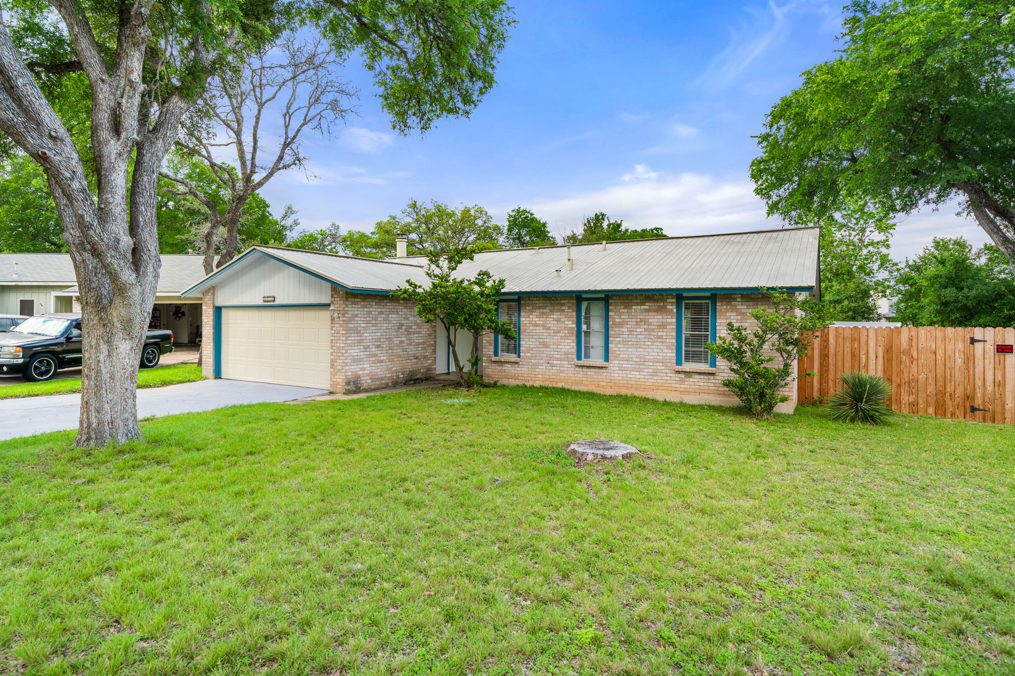 Ranch-style home featuring brick siding, a concrete driveway, an attached garage, and a metal roof with a towering tree