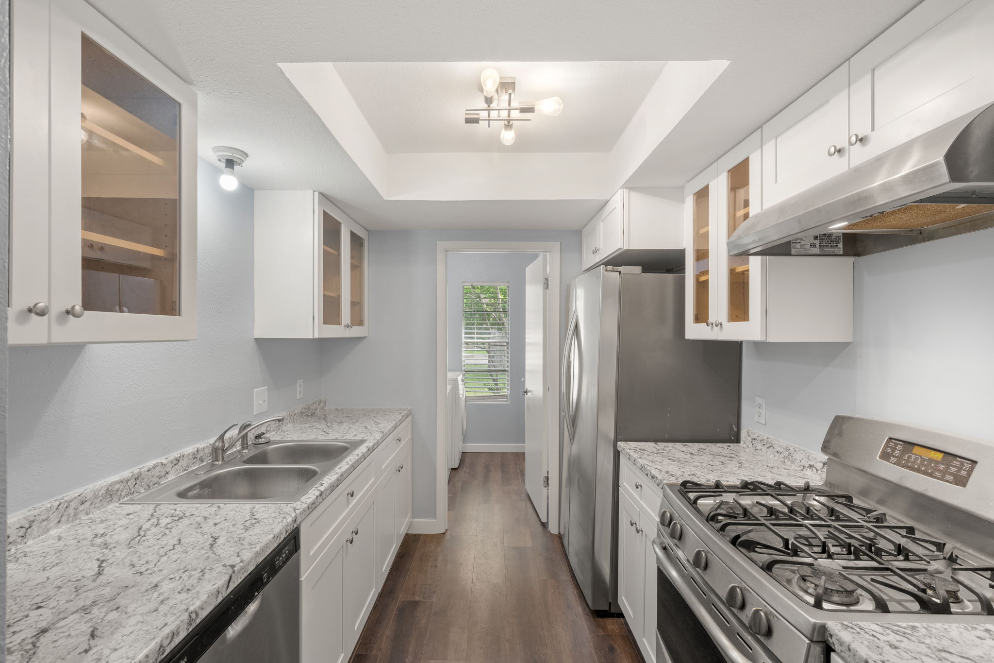 3917 Leafield Drive Austin, TX 78749 - Photo 4 of 40 Kitchen with glass insert cabinets, stainless steel appliances, white cabinetry, dark wood-style flooring, a tray ceiling and a laundry room off the kitchen