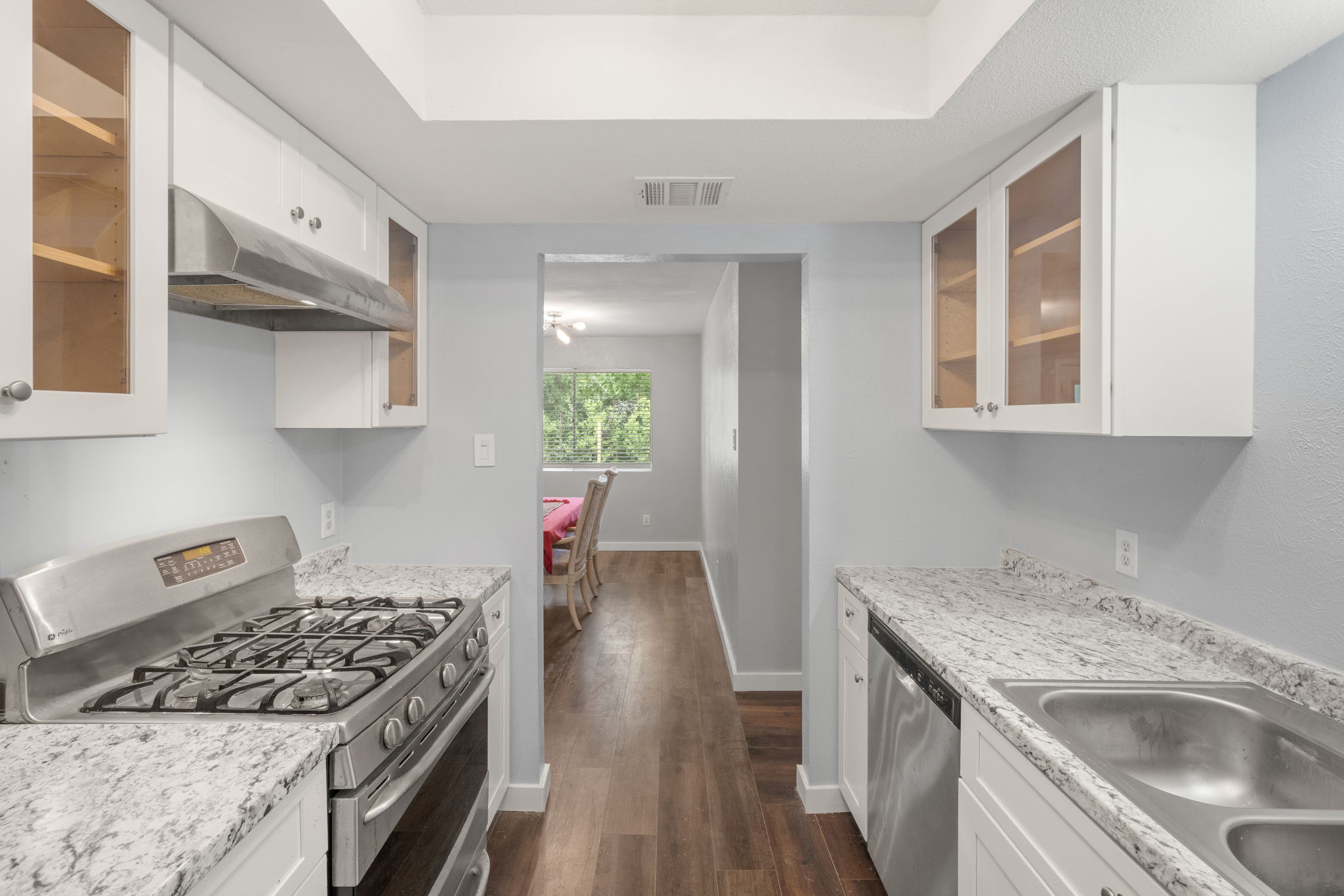 3917 Leafield Drive Austin, TX 78749 - Photo 6 of 40 Galley-style kitchen with glass insert cabinets, stainless steel appliances, white cabinets, dark wood-style floors, and a tray ceiling
