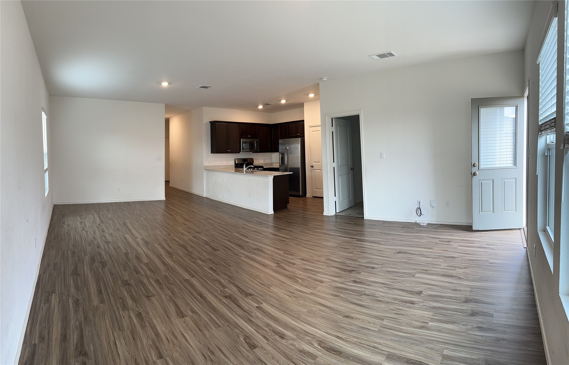 13501 Mussel Run Elgin, TX 78621 - Photo 8 of 28 Open-concept living space featuring wood-finish flooring, recessed lighting, and a kitchen with dark cabinetry and stainless steel appliances