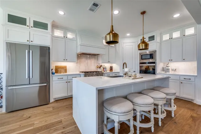 a kitchen with stainless steel appliances a sink a stove a refrigerator and chairs
