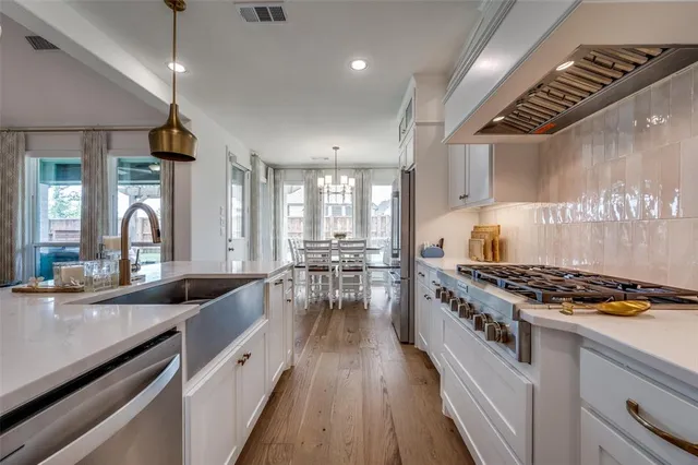 a kitchen with stainless steel appliances granite countertop a stove a sink dishwasher and white cabinets with wooden floor