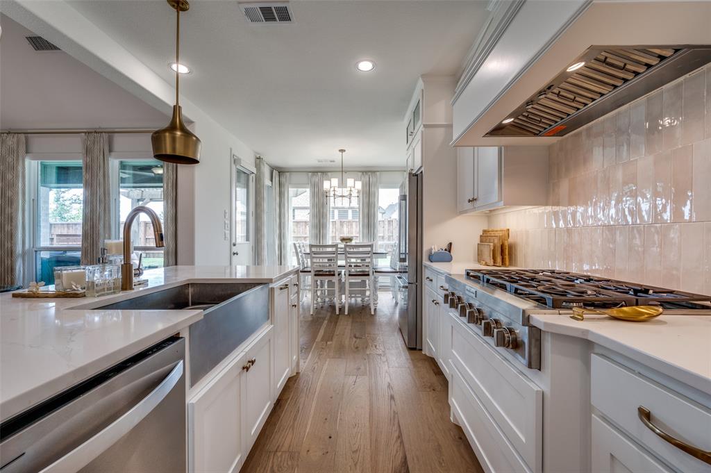 2390 Red Cedar Trail Prosper, TX 75078 - Photo 14 of 40 a kitchen with stainless steel appliances granite countertop a stove a sink dishwasher and white cabinets with wooden floor
