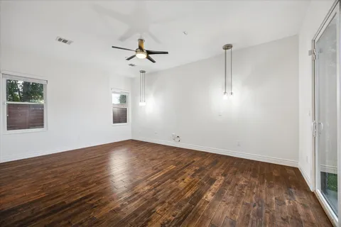 an empty room with wooden floor ceiling fan and windows