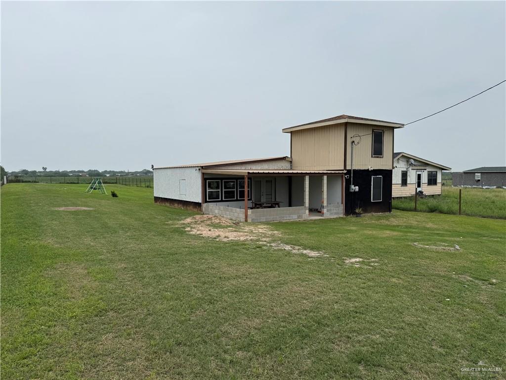 23265 Skinner Road Edcouch, TX 78538 - Photo 2 of 24 Property featuring a two-story structure with tan and black siding, a covered porch, and an expansive grassy yard