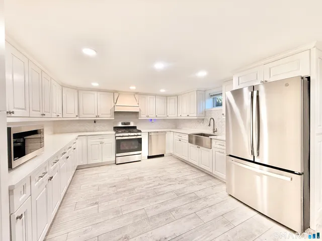 a large kitchen with stainless steel appliances kitchen island granite countertop a refrigerator oven a sink dishwasher and white cabinets with wooden floor