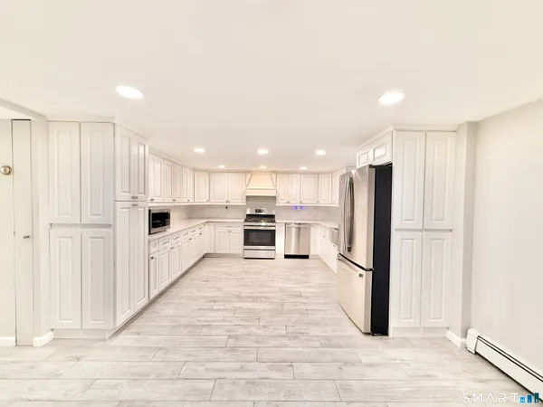 a large kitchen with stainless steel appliances kitchen island granite countertop a refrigerator oven a sink dishwasher and white cabinets with wooden floor