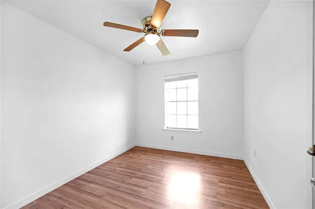 an empty room with wooden floor ceiling fan and windows