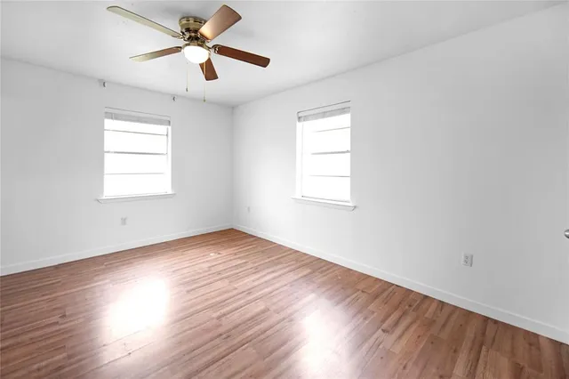 an empty room with wooden floor ceiling fan and windows