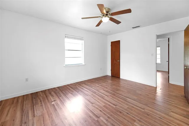 an empty room with wooden floor chandelier fan and windows
