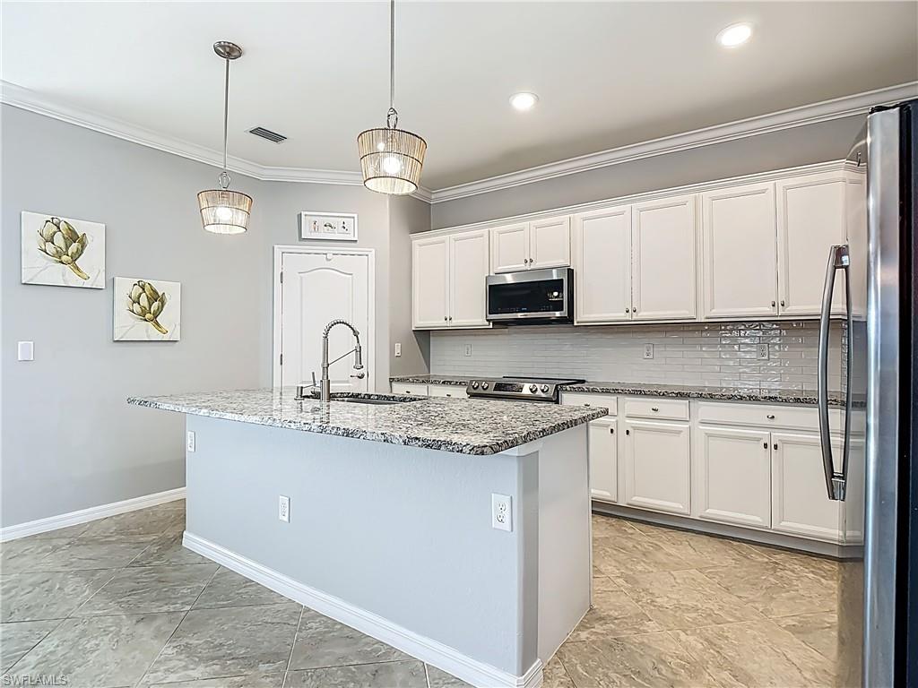 19890 Beverly Park Road Estero, FL 33928 - Photo 12 of 38 Kitchen featuring dark stone countertops, ornamental molding, stainless steel appliances, an island with sink, and white cabinetry