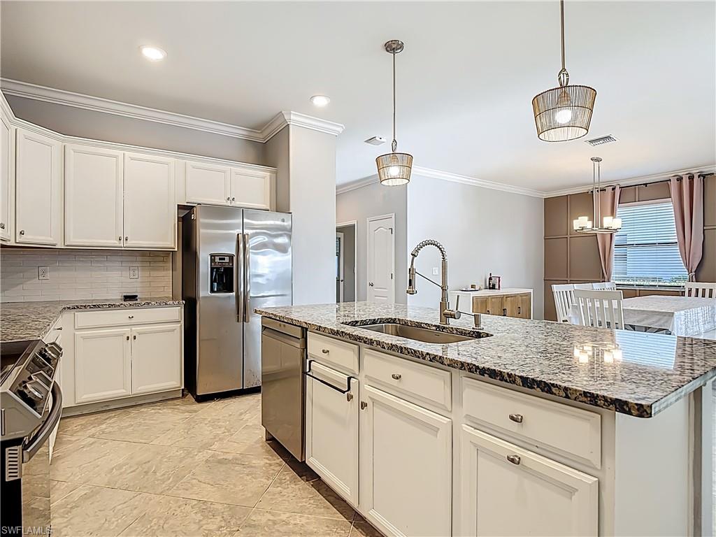 19890 Beverly Park Road Estero, FL 33928 - Photo 13 of 38 Kitchen with ornamental molding, appliances with stainless steel finishes, white cabinetry, a center island with sink, and light stone countertops