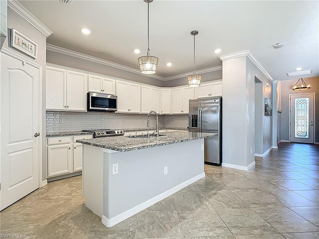 19890 Beverly Park Road Estero, FL 33928 - Photo 14 of 38 Kitchen with appliances with stainless steel finishes, decorative backsplash, an island with sink, ornamental molding, and hanging light fixtures
