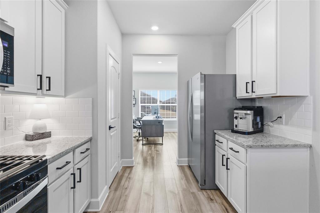 1012 Calhoun Drive Anna, TX 75409 - Photo 14 of 39 Kitchen corridor featuring white cabinetry with matte black hardware, stainless steel appliances, and light wood-finish flooring