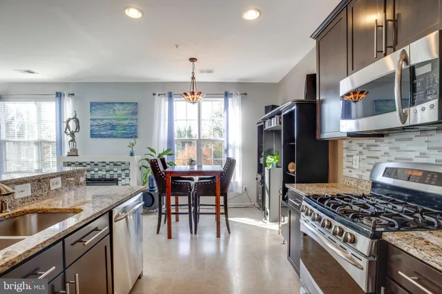 a kitchen with stainless steel appliances granite countertop a stove a refrigerator a sink a dining table and chairs with wooden floor