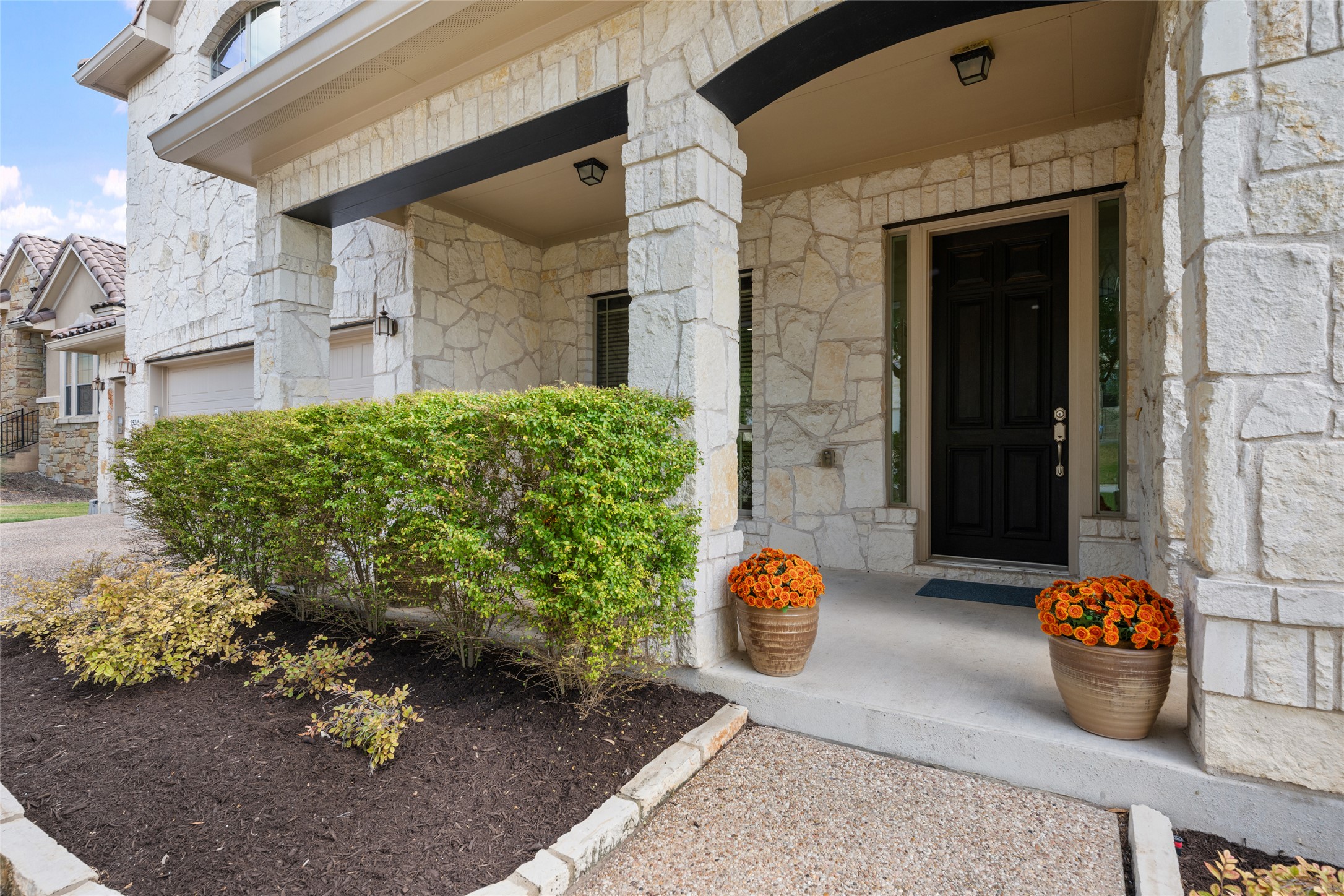 15205 Spillman Ranch Loop Austin, TX 78738 - Photo 3 of 40 A welcoming stone facade with a covered entry leads to a solid panel door, framed by verdant landscaping.