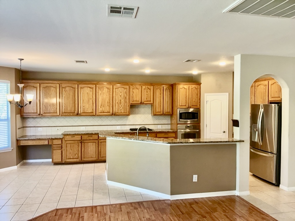 2518 Vestavia Ridge Lane Cedar Park, TX 78613 - Photo 5 of 23 Kitchen featuring stainless steel appliances, dark stone counters, light tile patterned floors, arched walkways, and wood finish cabinets
