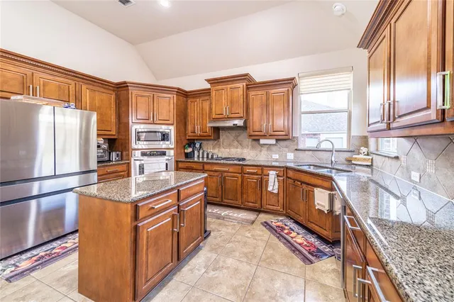 a kitchen with stainless steel appliances granite countertop a refrigerator a sink dishwasher a stove with wooden cabinets and floor