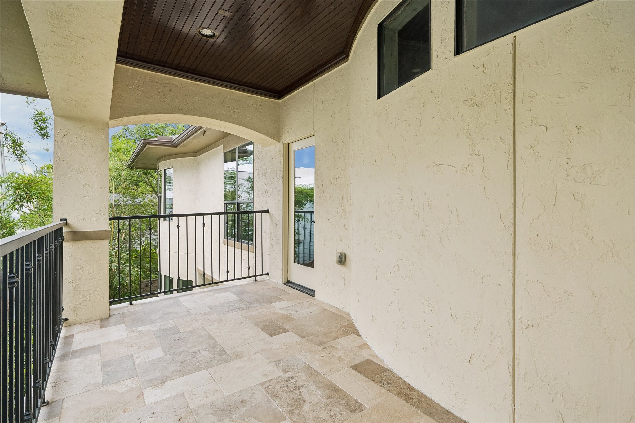2246 Branard Street Houston, TX 77098 - Photo 26 of 40 A covered private balcony off the primary suite with travertine flooring, wood-paneled ceiling detail, and serene treetop views.