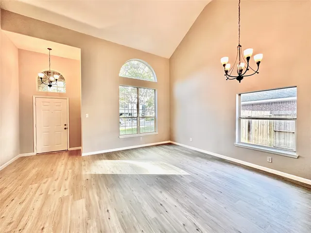 an empty room with wooden floor chandelier and windows