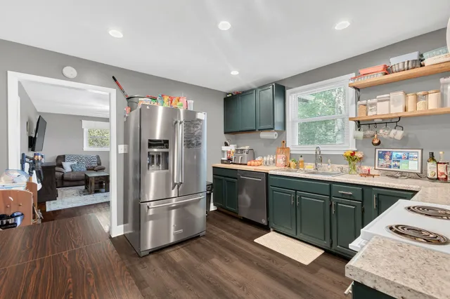 a kitchen with stainless steel appliances granite countertop a refrigerator a sink dishwasher a stove and white countertops with wooden floor