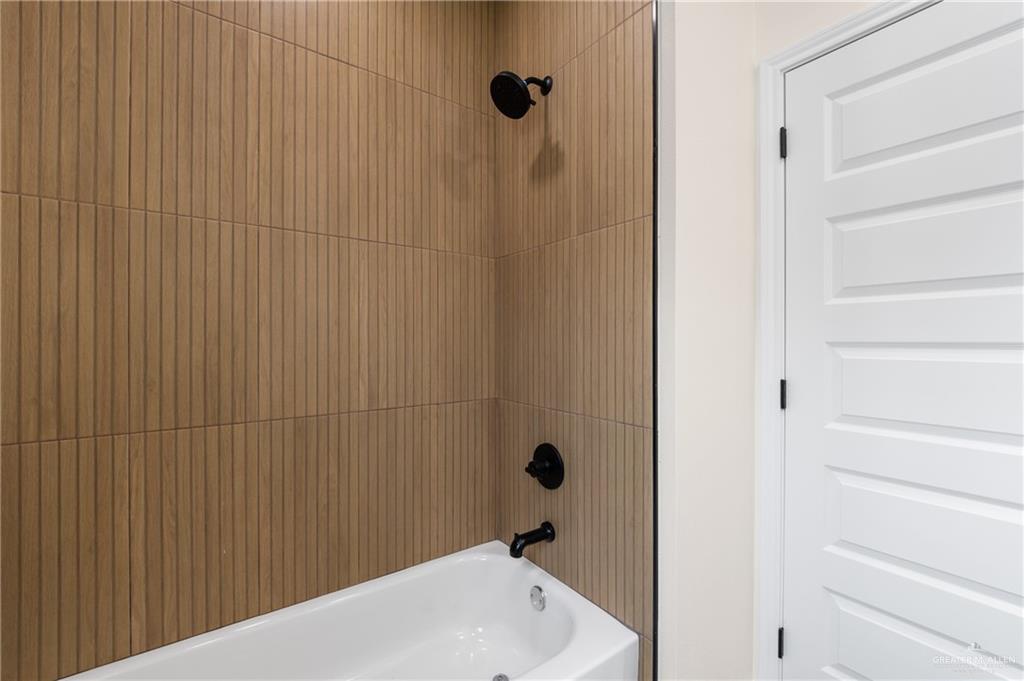 18054 Spruce Street Combes, TX 78552 - Photo 16 of 25 Bathtub and shower combination featuring floor-to-ceiling vertically-textured wood-finish tile, matte black shower fixtures, and a white paneled door
