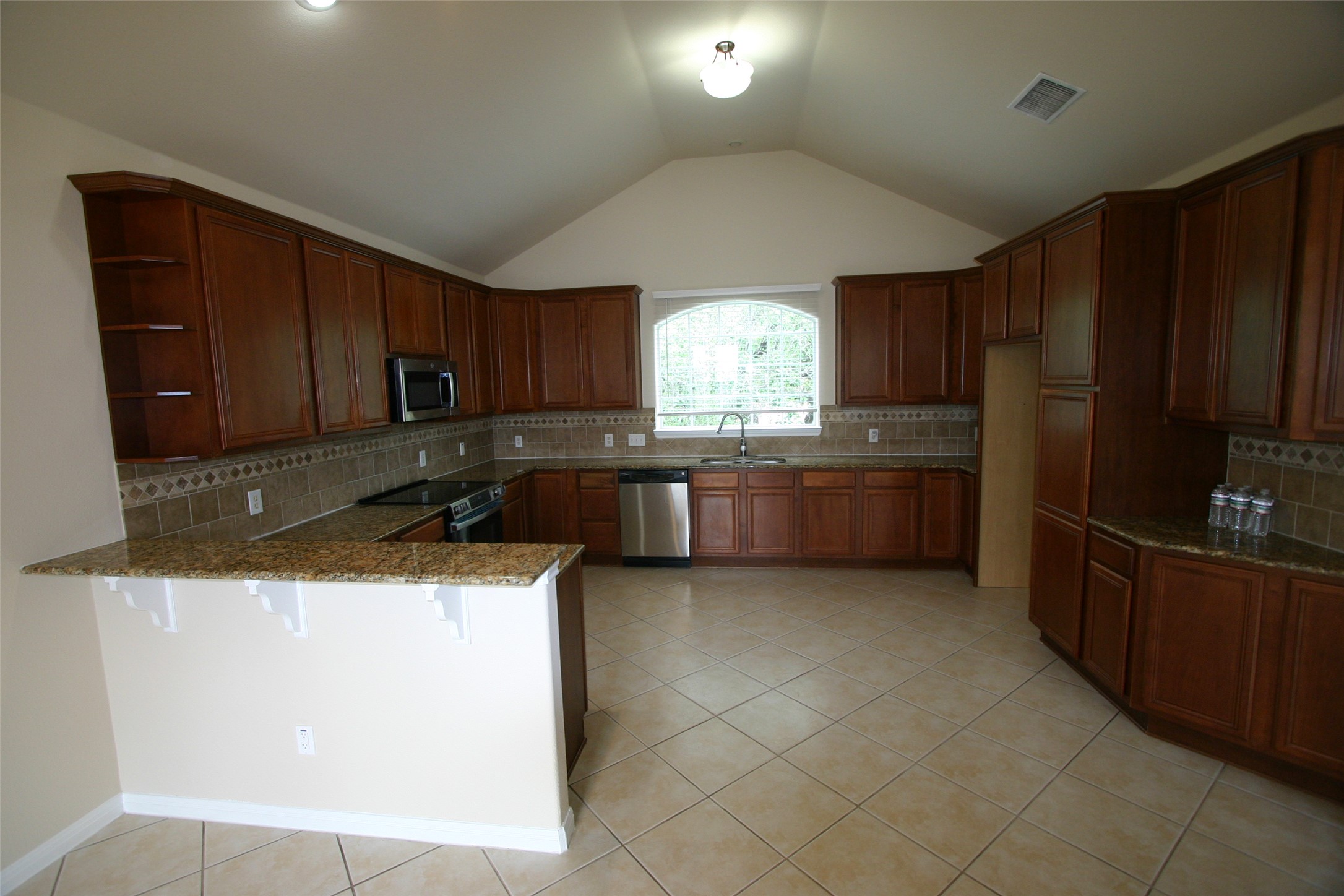Kitchen featuring a peninsula, decorative backsplash, a kitchen breakfast bar, dark stone countertops, and stainless steel appliances