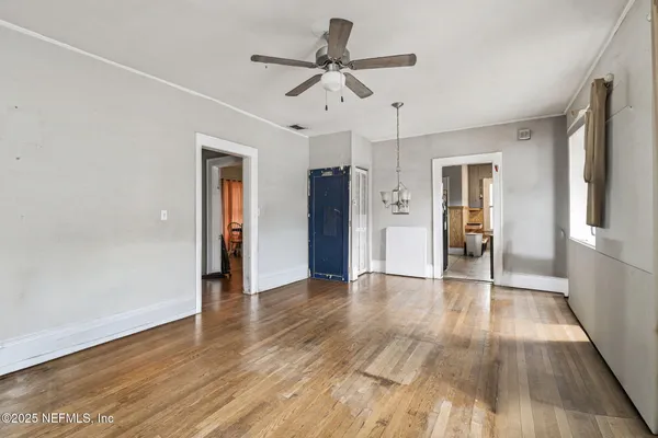 a view of an empty room with wooden floor and a ceiling fan