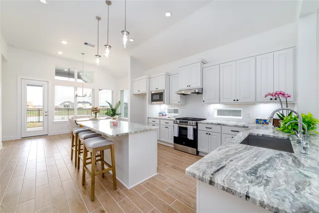 a kitchen with stainless steel appliances kitchen island granite countertop a stove a sink a refrigerator and a dining table with wooden floor