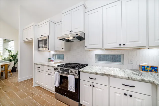 a kitchen with stainless steel appliances granite countertop a sink a stove and a white cabinets