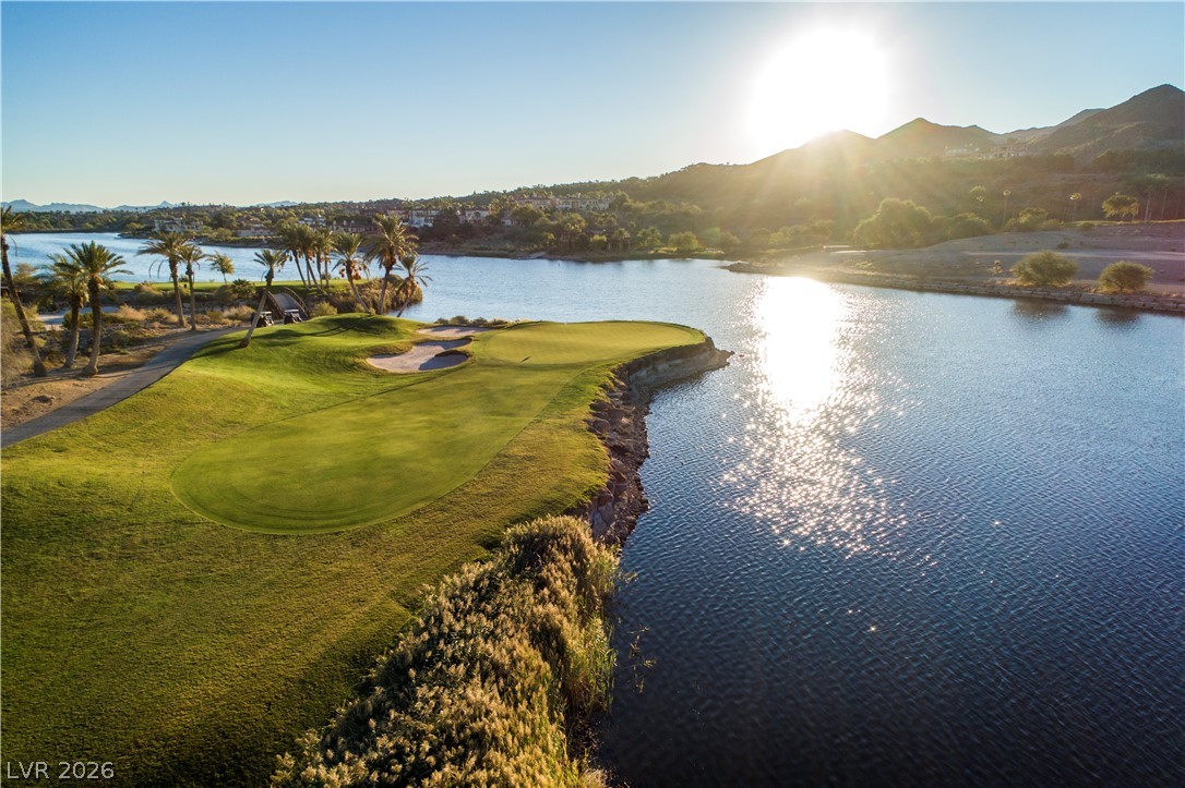 25 Falling Ridge Lane Henderson, NV 89011 - Photo 47 of 48 A golf course green, bunkers, and a cart path nestle beside a tranquil lake with sun-drenched mountains in the distance.